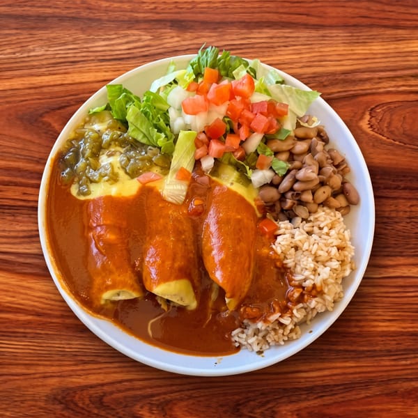 Three enchiladas with red sauce, green chili, rice, beans, and a fresh lettuce and tomato salad.