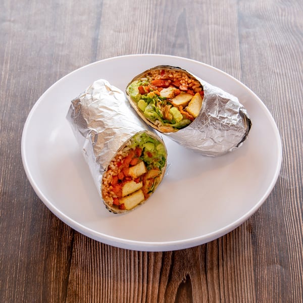 Two foil-wrapped burritos, cut in half to show fillings of rice, tofu, and guacamole, on a white plate.