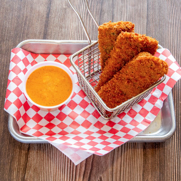 Fried pickles in a metal basket with a side of dipping sauce on a red and white checkered paper.